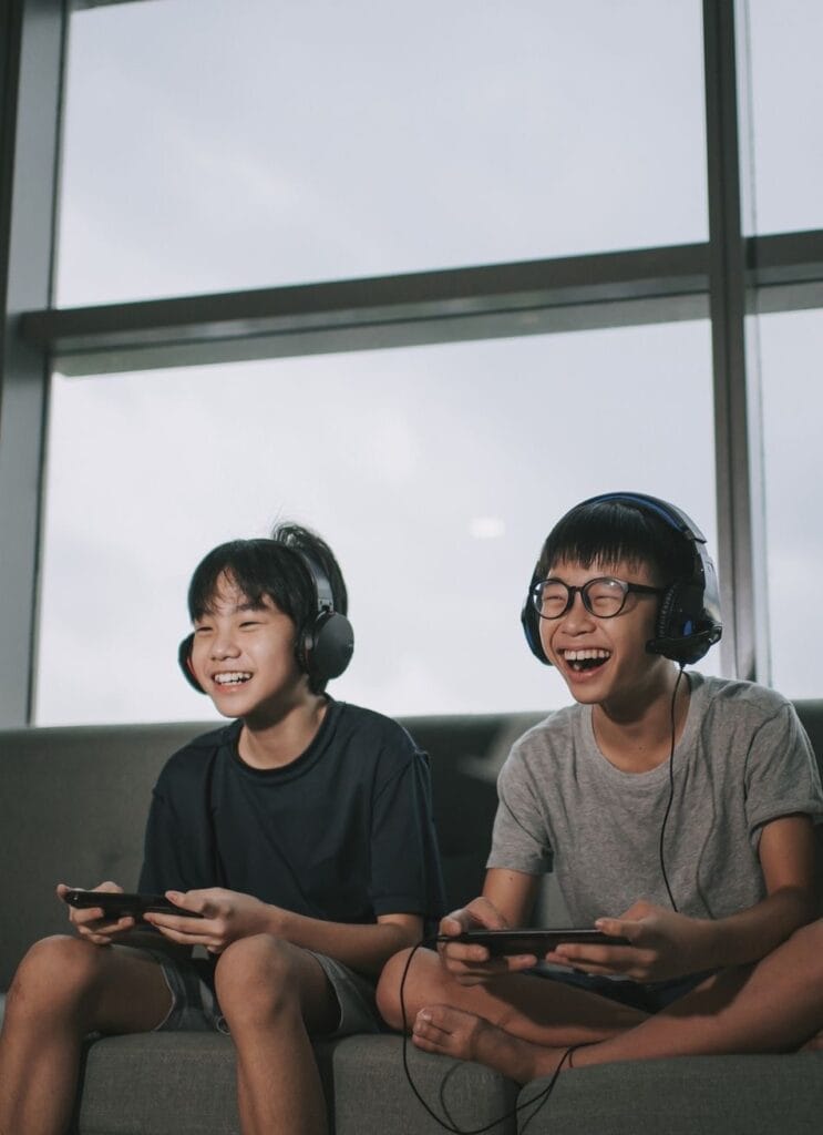 Two friends laughing and bonding while playing video games together, highlighting the importance of building genuine connections beyond the screen in social gaming.